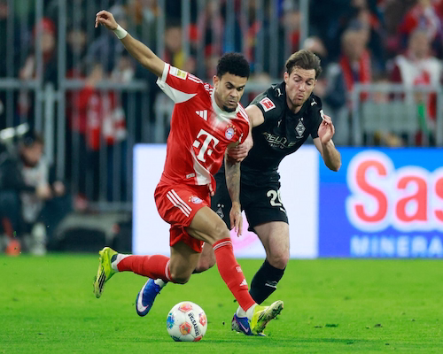 Luis Díaz conduce la pelota mientras un jugador de Borussia Mönchengladbach lo toma del brazo para intentar frenarlo durante un partido de la Bundesliga.