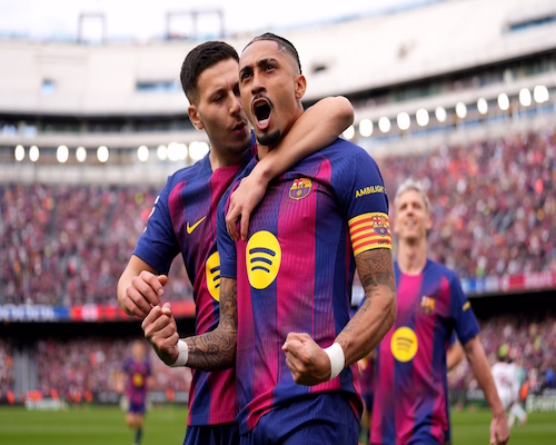 Raphinha celebra uno de sus goles con los puños cerrados mientras un compañero de Barcelona lo abraza por detrás durante el partido ante Sevilla por LaLiga.