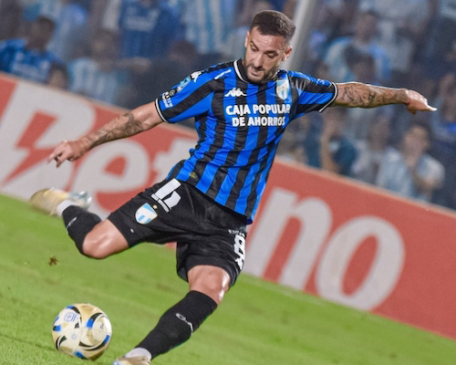 Jugador de Atlético Tucumán ejecuta un remate de zurda durante un partido nocturno