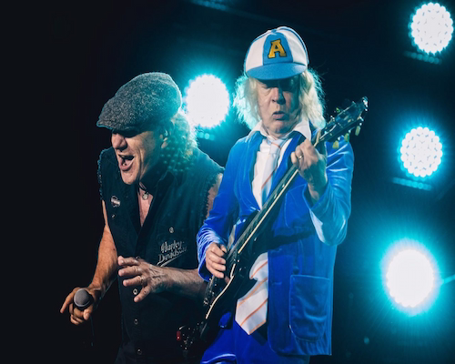 Primer plano de Brian Johnson cantando y Angus Young tocando la guitarra, iluminados por intensas luces de escenario