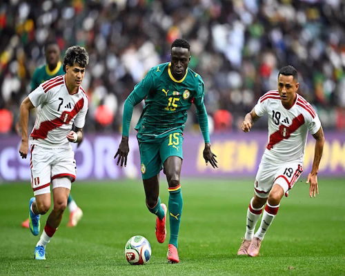 Jugador de Senegal conduce la pelota ante la marca de dos futbolistas de Perú durante un amistoso internacional