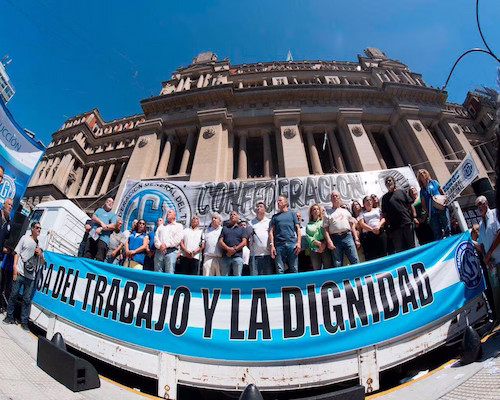 Dirigentes sindicales y trabajadores concentrados frente a un edificio público con banderas y una pancarta en defensa del trabajo y la dignidad