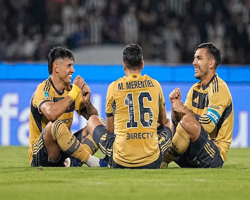 Jugadores de Boca Juniors festejando un gol sentados y tomados de las manos en el campo de juego