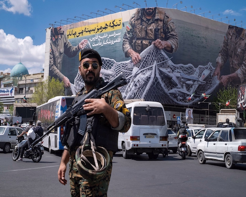 Militar armado patrulla una calle en Irán frente a un gran mural propagandístico relacionado con el Estrecho de Ormuz