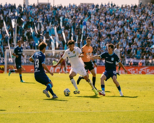 Agustín Palavecino conduce el balón mientras es presionado por dos jugadores de Racing Club