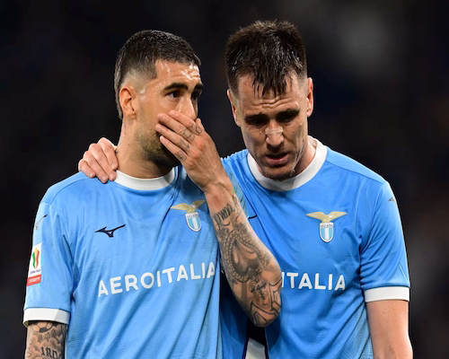 Jugadores de Lazio dialogan en el campo de juego durante el partido, uno de ellos con la mano cubriéndose la boca.