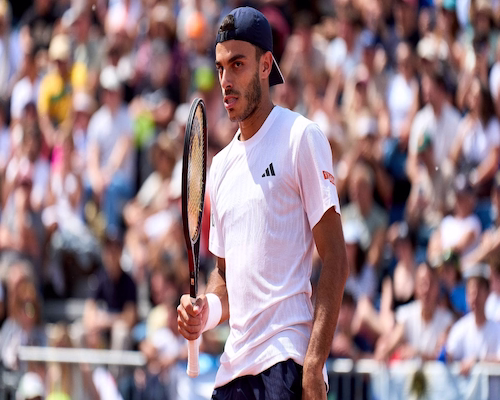 Francisco Cerúndolo con camiseta blanca y gorra azul marino sostiene su raqueta en la mano derecha frente a las gradas del Madrid Open