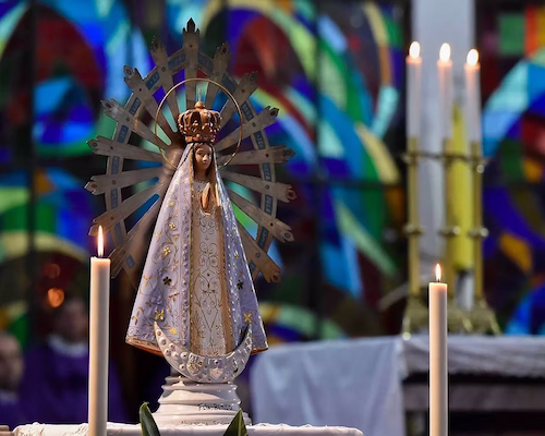 Imagen de la Virgen de Nuestra Señora de Luján sobre un altar con velas encendidas y vitrales de fondo