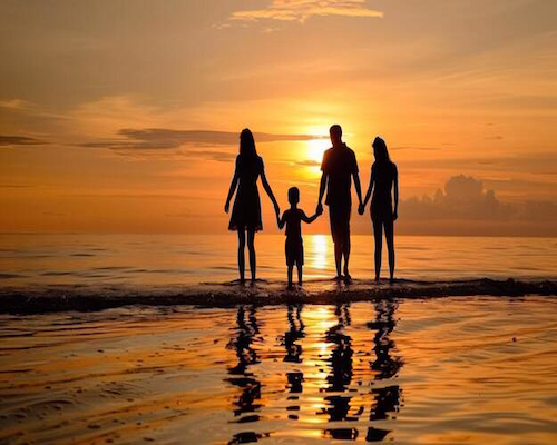 Una familia caminando tomada de la mano sobre la playa durante el atardecer