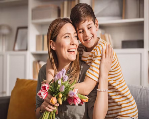 Hijo abranzando a su madre que sostiene un ramo de flores en la mano