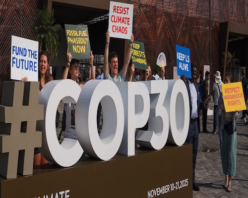 Activistas climáticos protestan frente al cartel de la COP30 en Belém con carteles sobre financiamiento, combustibles fósiles y derechos indígenas.