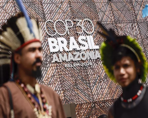 Personas con vestimentas tradicionales frente al cartel oficial de la COP30 en Belém durante el cierre de la cumbre climática.