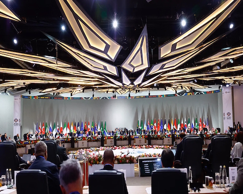 Vista general de la sesión plenaria del G20 con delegaciones internacionales reunidas en una mesa circular rodeada de banderas de los países miembros.
