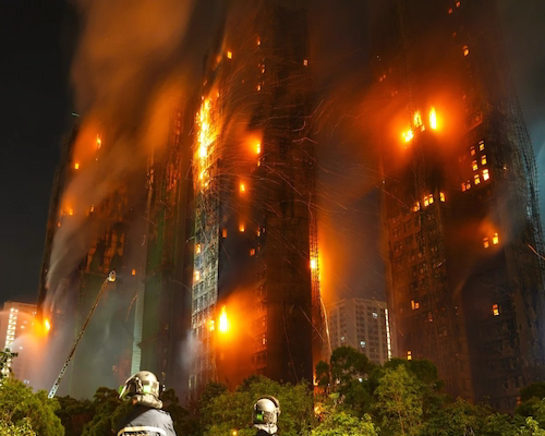 Torres residenciales envueltas en llamas durante un incendio nocturno, con bomberos trabajando en primer plano.