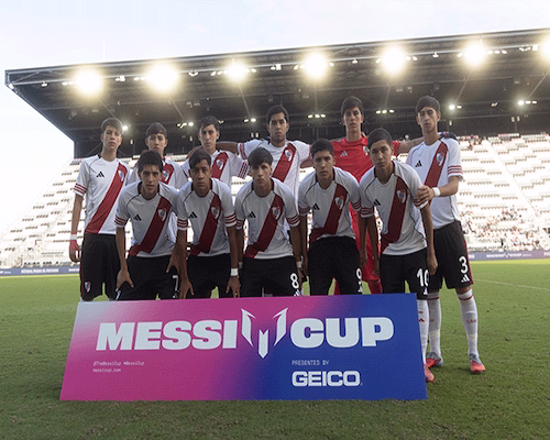 Plantel juvenil de River Plate posa en el campo de juego antes de un partido de la Messi Cup, con el cartel oficial del torneo al frente.