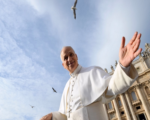 El Pontífice saluda con la mano desde la Plaza de San Pedro, vestido con sotana blanca, bajo un cielo despejado con aves en vuelo.