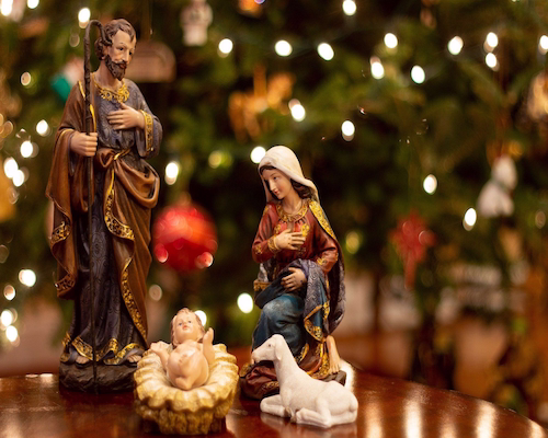 Nacimiento de Jesús con las figuras de María y José frente a un árbol de Navidad iluminado.