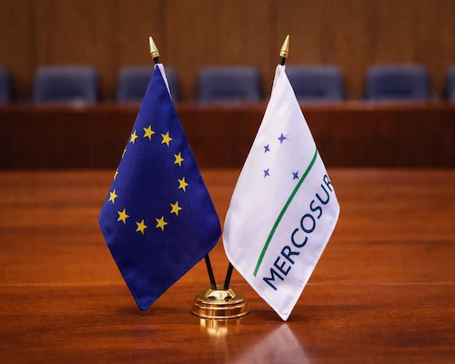 Banderas de la Unión Europea y del Mercosur colocadas sobre una mesa durante una reunión institucional.