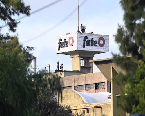 Planta de la fábrica de neumáticos Fate con su logo visible en lo alto del edificio y trabajadores sobre la estructura tras el anuncio de cierre.