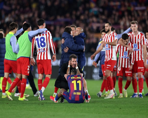 Raphinha sentado en el césped es consolado por Diego Simeone mientras jugadores de Atlético de Madrid celebran la clasificación a la final de la Copa del Rey.