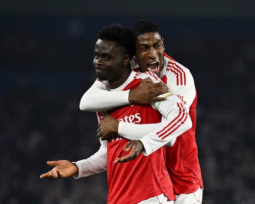 Bukayo Saka celebra su gol con un encogimiento de hombros y las palmas hacia arriba mientras Cristhian Mosquera lo abraza por la espalda.