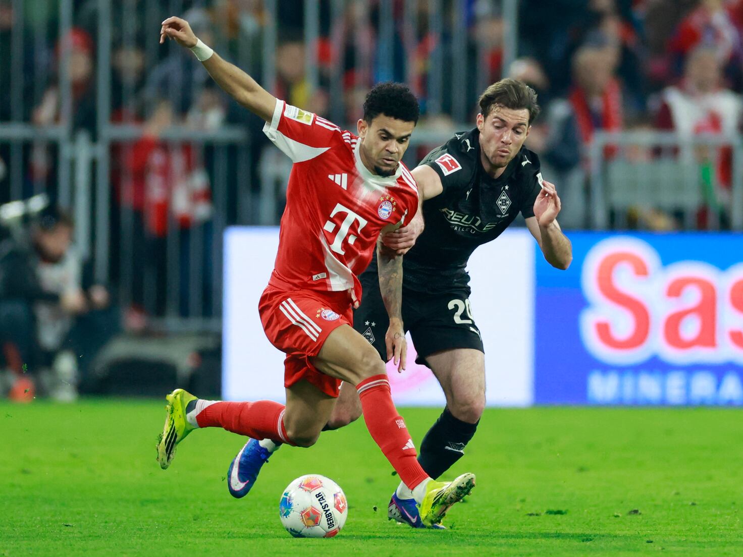 Luis Díaz conduce la pelota mientras un jugador de Borussia Mönchengladbach lo toma del brazo para intentar frenarlo durante un partido de la Bundesliga.