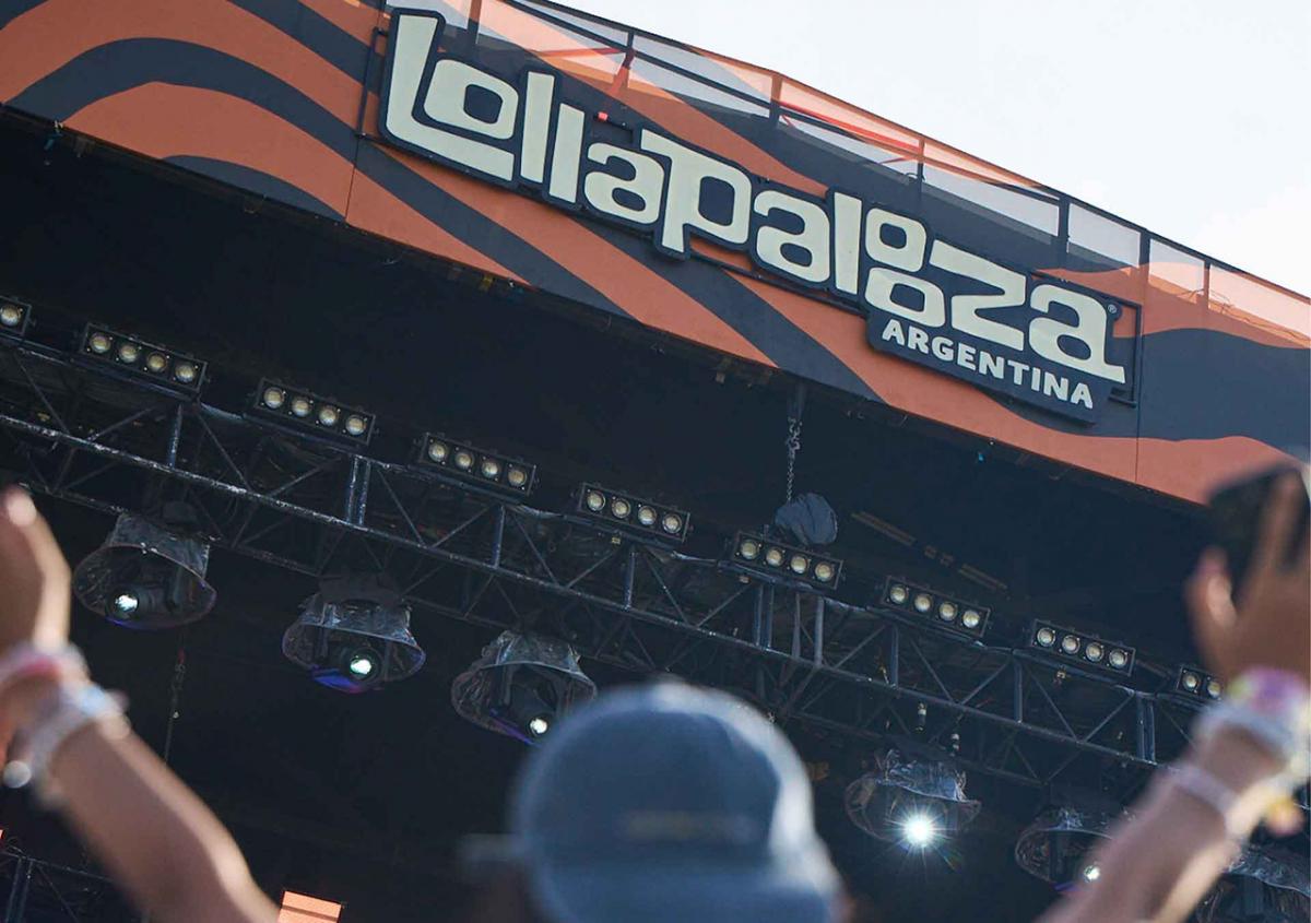 Escenario principal del festival Lollapalooza Argentina con el cartel del evento mientras una persona levanta las manos durante un show.