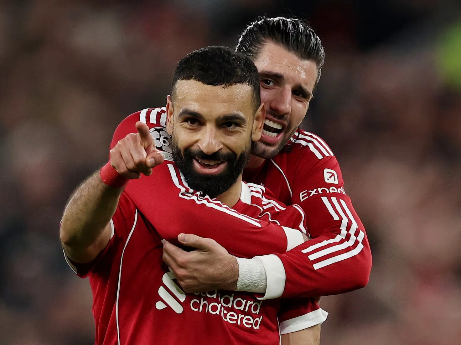Mohamed Salah sonríe y señala hacia adelante mientras Dominik Szoboszlai lo abraza por detrás tras un gol de Liverpool