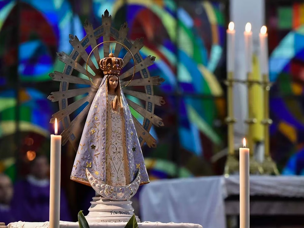 Imagen de la Virgen de Nuestra Señora de Luján sobre un altar con velas encendidas y vitrales de fondo