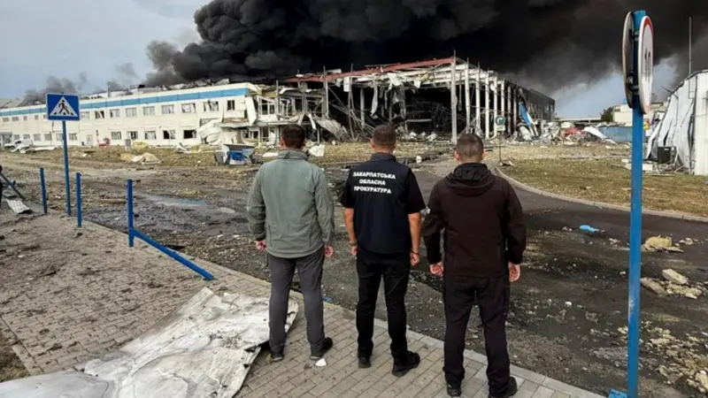 Tres hombres de espalda observando como un edificio se quema y lanza una enorme columna de humo negro