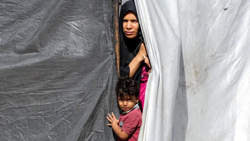 Una mujer y un niño se asoman desde una tienda de campaña en Gaza.