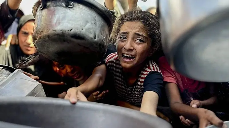 Niña luchando por recibir un plato comida en Gaza.