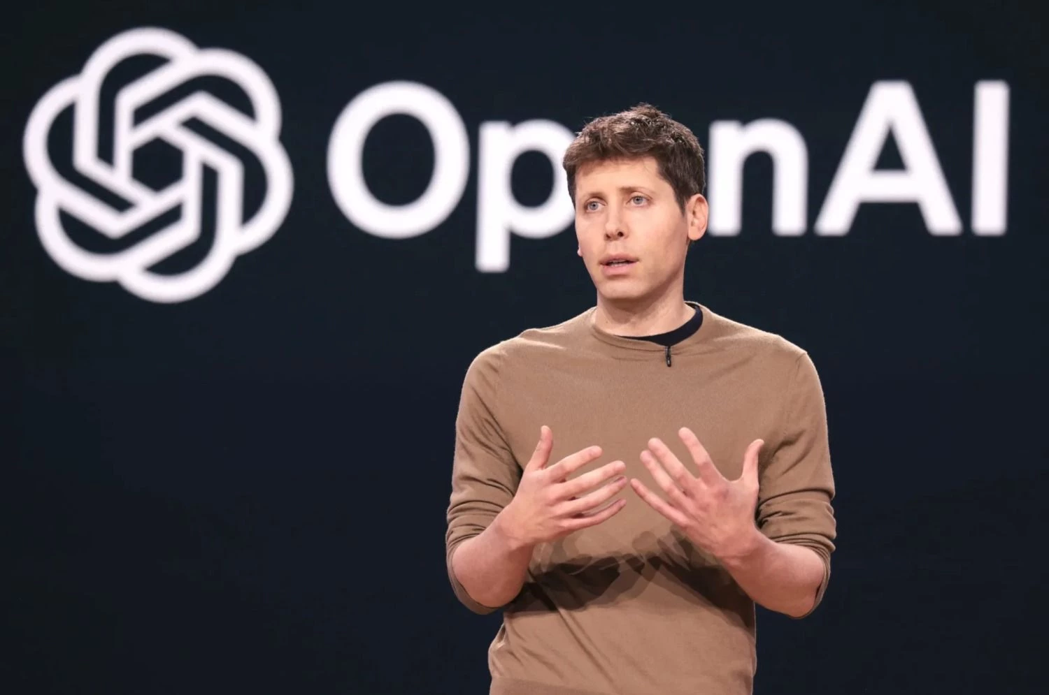 Sam Altman, CEO de OpenAI, dando una presentación frente al logo de la empresa