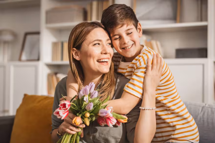 Hijo abranzando a su madre que sostiene un ramo de flores en la mano