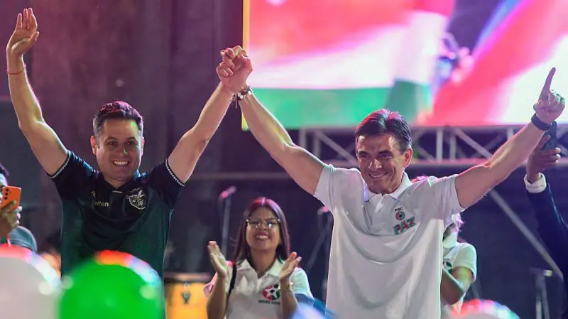 La fórmula presidencial Rodrigo Paz y Edmand Lara celebran sobre un escenario con los brazos arriba.