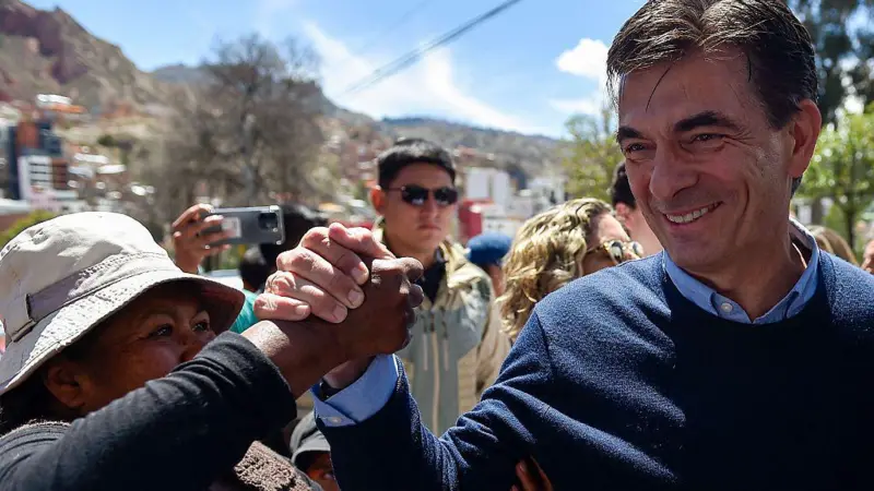 Rodrigo Paz sonríe tomando la mano de una mujer que lo mira con entusiasmo.