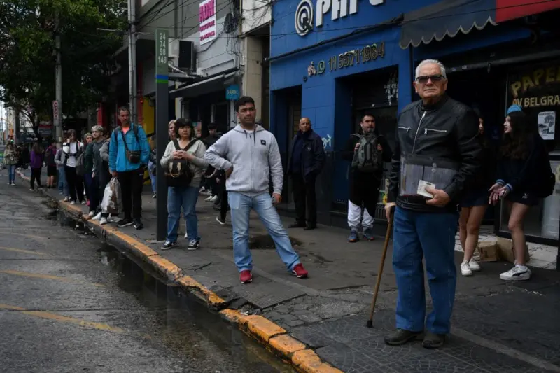 Un grupo de personas espera un autobús parados en la vereda de una avenida en Buenos Aires.