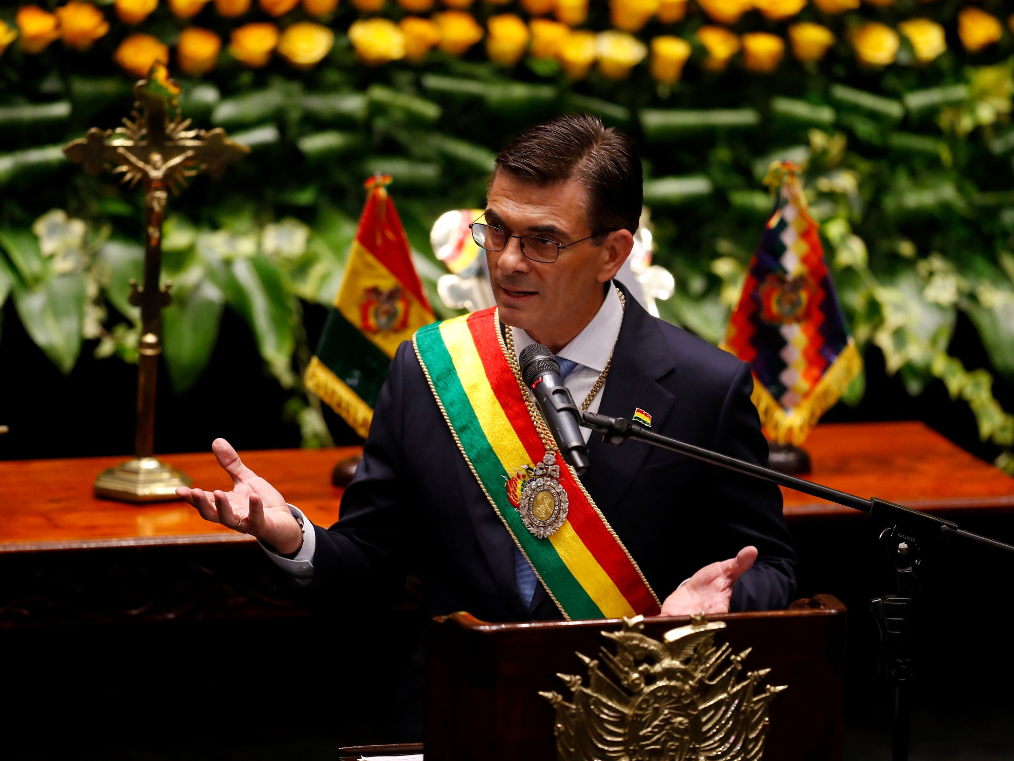 Rodrigo Paz lavanta las palmas de las manos hacia arriba delante de un atril con la banda presidencial sobre sus hombros.