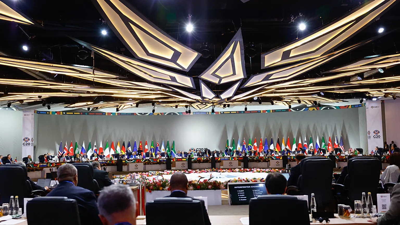 Vista general de la sesión plenaria del G20 con delegaciones internacionales reunidas en una mesa circular rodeada de banderas de los países miembros.