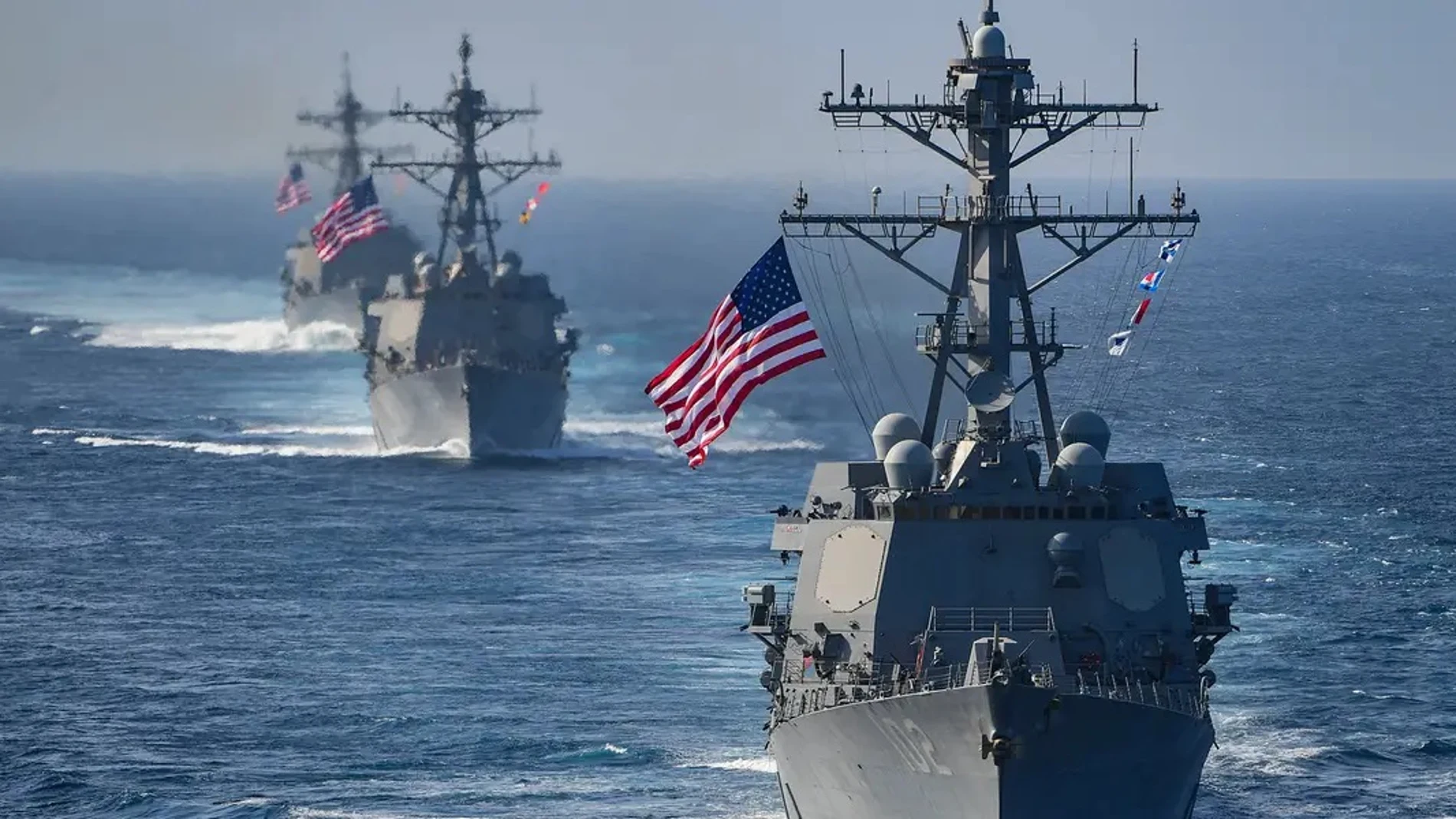 Buques de guerra de la Armada de Estados Unidos navegan en formación en aguas de Medio Oriente con banderas estadounidenses izadas.