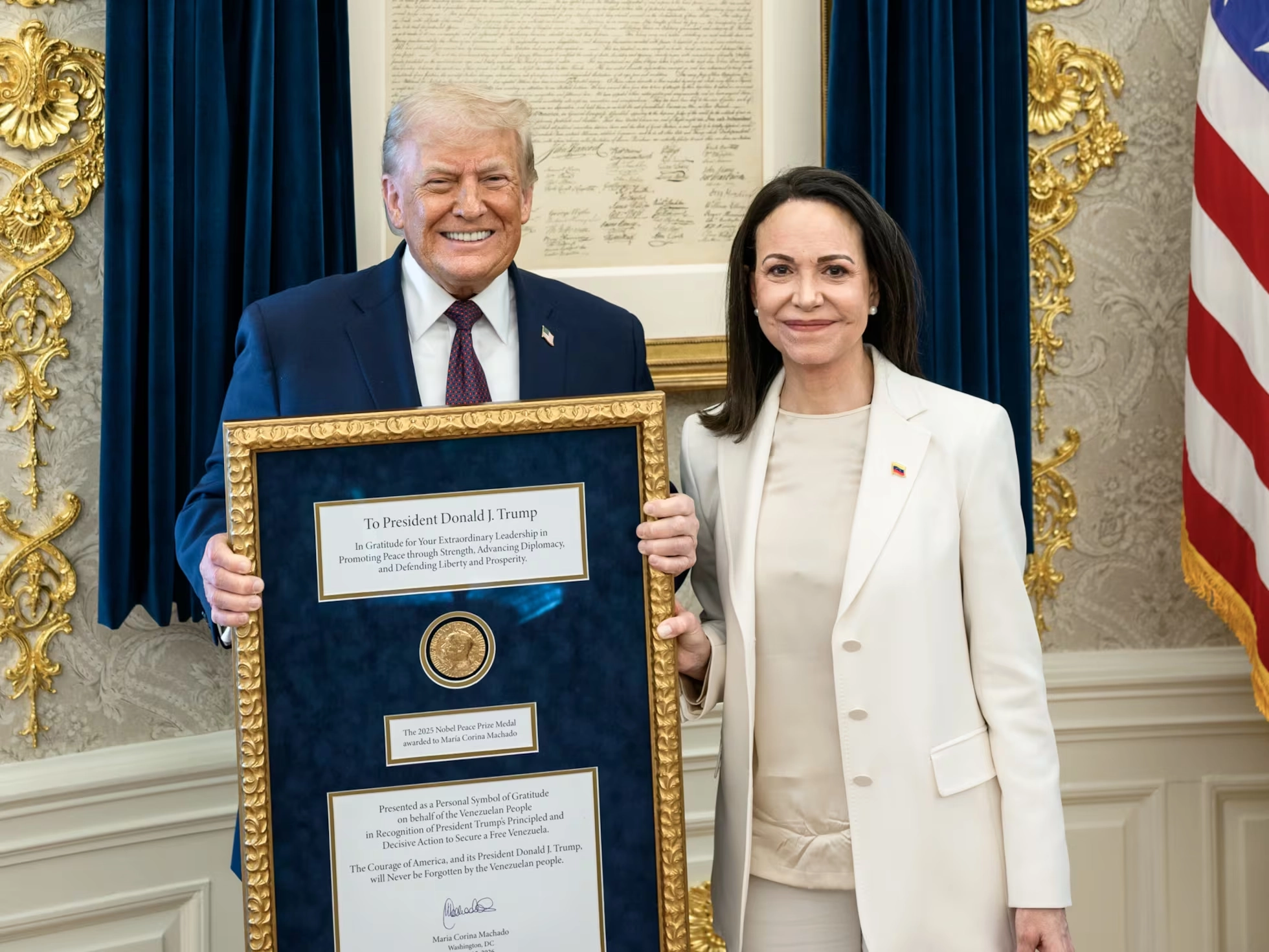Dirigente opositora venezolana y presidente de Estados Unidos posan en la Casa Blanca mientras sostienen un cuadro con la medalla del Premio Nobel de la Paz.