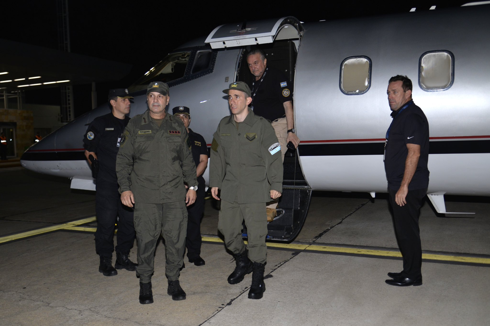 El gendarme Nahuel Gallo descendiendo de un avión privado en el Aeropuerto de Ezeiza tras su liberación en Venezuela, acompañado por oficiales de seguridad y personal de AFA.