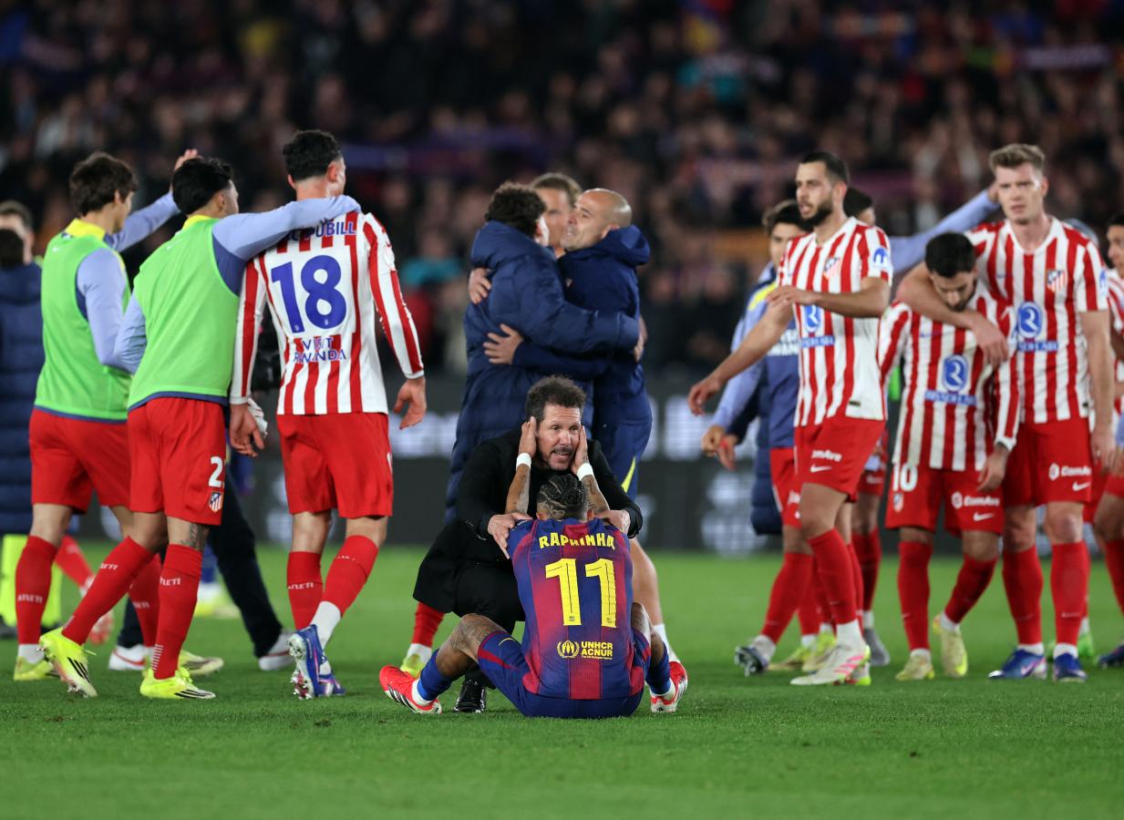 Raphinha sentado en el césped es consolado por Diego Simeone mientras jugadores de Atlético de Madrid celebran la clasificación a la final de la Copa del Rey.